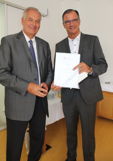 Paul Meuer und Bürgermeister Winfried Steinmacher in dunklen Anzügen und Herr Steinmacher mit weißer Ernennungsurkunde zum Vorsitzenden des Vorstandes der Stiftung Lebensraum Rheingau-Taunus.