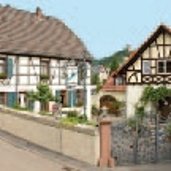 Zwei beige Fachwerkhäuser  mit braunen Balken und eine beige Mauer mit verziertem Metalltor und Innenhof mit Topfpflanzen