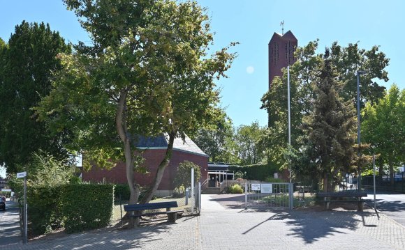 Kirchturm und Gebäude aus roten Steinen der Evangelische Kirche Kiedrich und Bäumen.