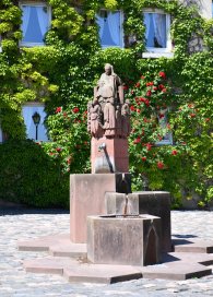 Steinbrunnen mit drei Becken und Figuren auf dem Kiedricher Marktplatz vor einem mit Efeu bewachsenem Haus