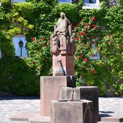 Steinbrunnen mit drei Becken und Figuren auf dem Kiedricher Marktplatz vor einem mit Efeu bewachsenem Haus