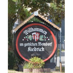Altes Weinfass aus Holz mit Begrüßungstext und Kiedricher Wappen mit Trauben und roter Umrandung sowie einem Schutzdach.