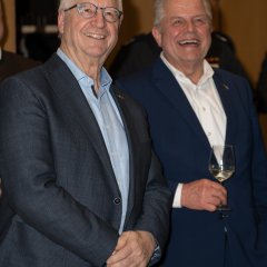 Manfred Schmidt, Ehrenvorsitzender des Sportkreis Rheingau-Taunus (links) mit Brille und dunklem Anzug und hellblauem Hemd mit Klaus-Peter Willsch, Abgeordneter im Deutschen Bundestag (rechts), mit dunklem Anzug und weißem Hemd und Weinglas in der Hand.