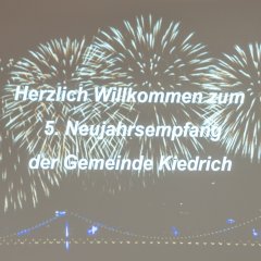 Auf einer großen Leinwand ist ein Feuerwerk mit vier großen goldenene Kreisen und unterhalb eine beleuchtete Brücke zu erkennen. 