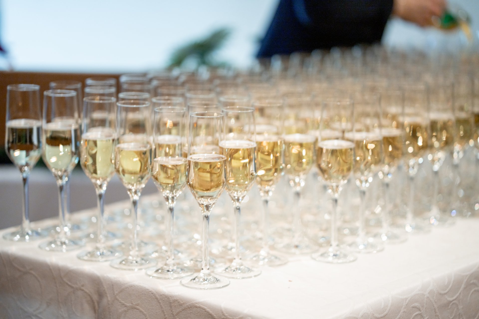 Auf eine langem Tisch mit einer weißen Stoff-Tischdecke stehen viele mit Sekt gefüllte Sektgläser.