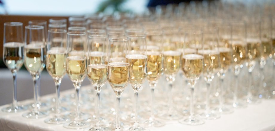 Auf eine langem Tisch mit einer weißen Stoff-Tischdecke stehen viele mit Sekt gefüllte Sektgläser.