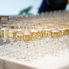 Auf eine langem Tisch mit einer weißen Stoff-Tischdecke stehen viele mit Sekt gefüllte Sektgläser.