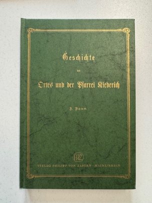 Auf einem grünem Untergrund ist ein goldener Rahmen und in goldenen Buchstaben steht in altdeutscher Schrift der Buchtitel "Geschichte des Ortes und der Pfarrei Kiedrich."