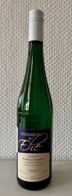 Eine dunkelgrüne Weinflasche, mit Erhebungen am Flaschenhals, Streifen, mit beige-blauem Etikett mit weißer, schwarzer und goldener Schrift und weißem Aluschrauber, steht vor einer weißen Strukturtapete.