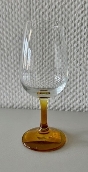 Ein Weinkelch mit braunem Stil steht vor einer weiße Strukturtapete.