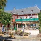 Weißes Fachwerkhaus mit braunen Balken einem breiten Balkon im ersten Stock, einer kleinen Balkonterrasse Terasse hinter dem bestuhltem Markplatz mit Marktbrunnen.