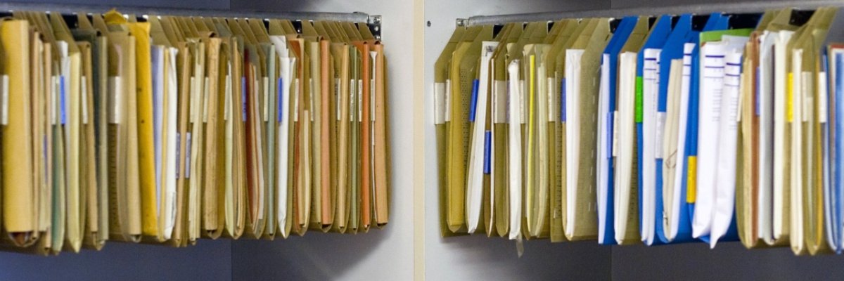 Offene Regale im rechten Winkel zueinander, in denen beige, gefüllte Registermappen hängen. 