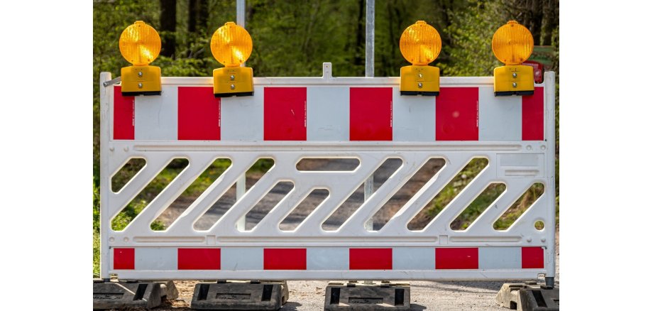 Eine Warnbake mit rot-weißen Streifen, aufgestellt auf vier grauen Ständern mit vier gelben Warnleuchten oberhalb des Schrankenzaunes.