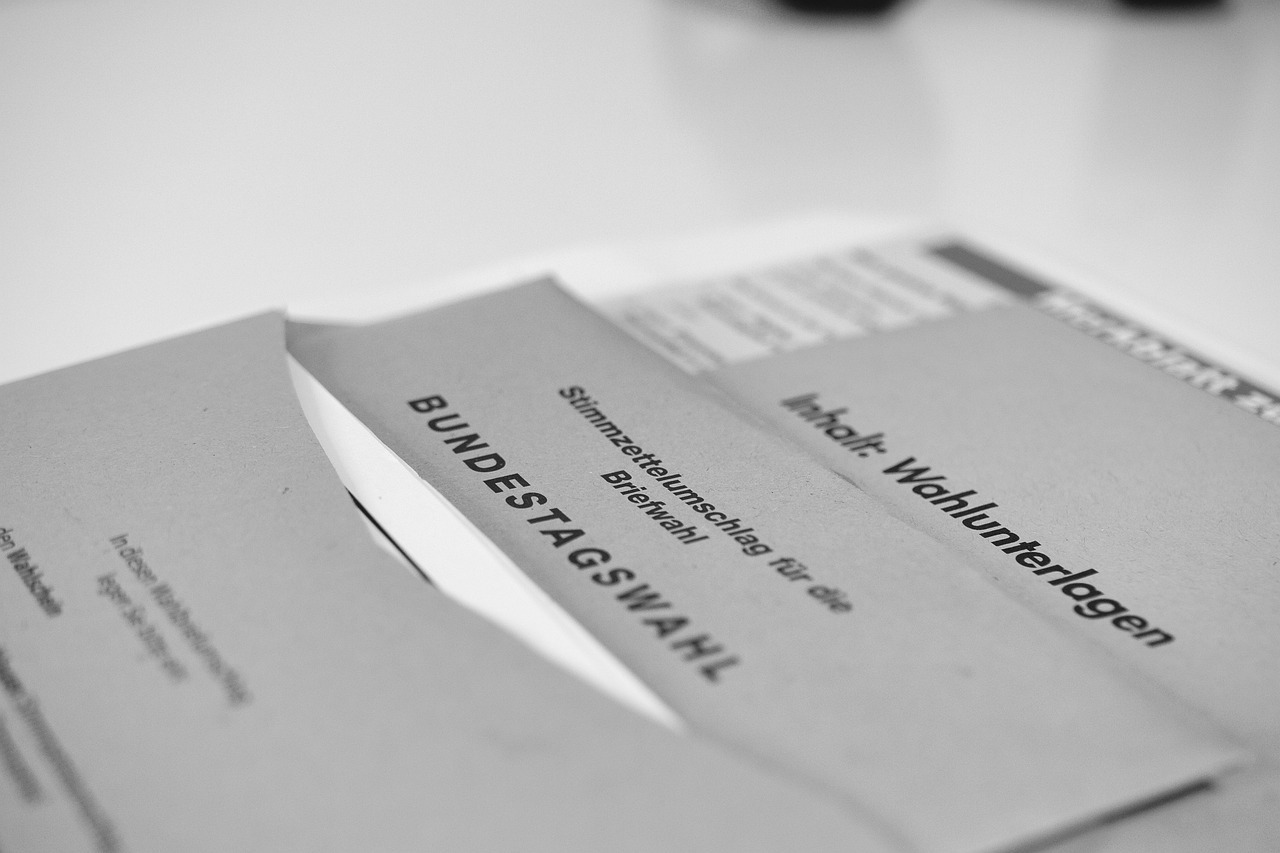 Auf einem grauen Tisch liegen mehrere graue Briefumschläge mit der Beschriftung Bundestagswahl und einem weißem Zettel. Ganz unten im Stapel ist ein Formular.