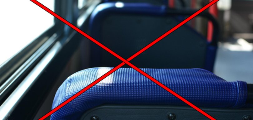Man sieht verschwommen einen Ausschnitt des Inneren eines Linienbusses, d.h. vier Sitze mit blauem Stoff und grauer Rückseite und rote Haltestangen. Links ist eine breite Fensterreihe zu erkennen. Über dem Bild sind zwei rote Linien, die sich kreuzen.