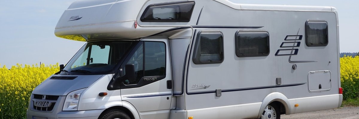 Vor einem blühendem Rapsfeld steht am Straßenrand ein Wohnmobil geparkt.