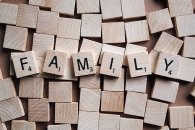 Familie Mehrere Vierecke aus Holz liegen durcheinander auf einer holzfarbenen Platte. Auf den Vierecken liegen weitere Vierecke aus Holz, von denen jedes  Viereck einen schwarzen Großbuchstaben und rechts unten eine kleine schwarze Zahl besitzt. Die Buchstaben ergeben das Wort "Family".