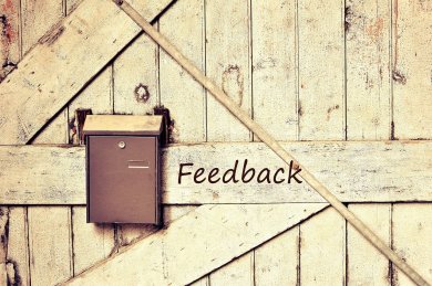 Feedback Auf einer Wand mit geraden und schrägen Holzbalken, hängt ein brauner Metallbriefkasten. Rechts davon steht Feedback.