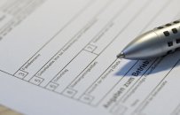 Auf einem weißen Formular, in dem mit schwarzen Rahmen Felder gedruckt sind mit diversen Bezeichnungen, liegt ein silberner Kugelschreiber, bei dem die Mine draussen ist und  schwarze kleine Vierecke an der Stelle sind, wo man ihn mit den Fingern festhält.