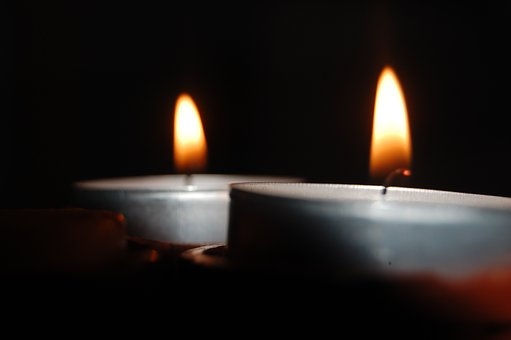 Zwei brennende Teelichter mit silberner Aluminiumschale vor schwarzem Hintergrund.  