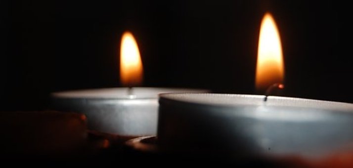 Zwei brennende Teelichter mit silberner Aluminiumschale vor schwarzem Hintergrund.  