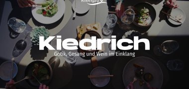Ein Rechteck ist auf einem Bild mit Wellen. Auf dem kleineren Rechteck sind Weinberg, ein Weg, der dadurch führt und auf dem Wanderer laufen und am Wegesrand stehen mit Abstand drei Bäume. Im HIntergrund ist der Wald zu sehen. Oben rechts ist eine Briefmarke, auf der eine Kirche abgebildet ist.