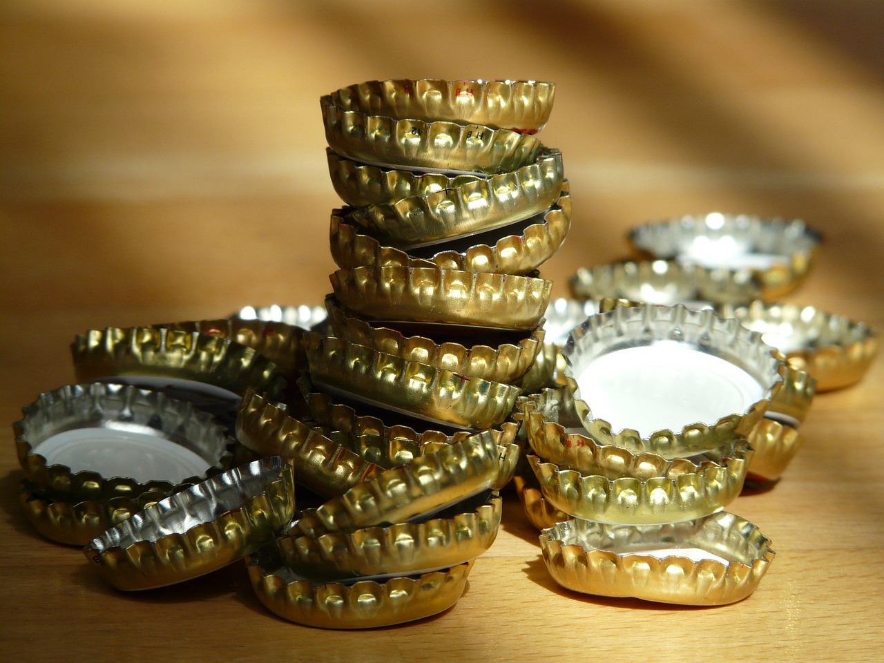 Auf einer braunen Holzfläche liegen goldene Kronkorken, quer übereinander und 14 Kronkorken wuren aufeinander gestapelt.