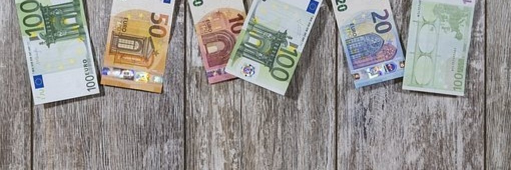Vor einer Wand mit Holzleisten hängt eine Kordel mit Holzklammern, an denen Geldschein aufgehängt sind. Drei 100 EUR-Scheine, ein  50 EUR-Schein, ein 20 EUR-Schein und ein 10 EUR-Schein. 