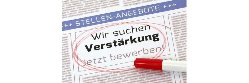 Auf einer Seite einer Zeitung ist eine blaue Überschrift mit Pluszeichen und in Großbuchstaben steht "Stellen-Angebote". Darunter der Text "Wir suchen Verstärkung-  Jetzt bewerben!".Dieser TExt ist rot umkreist. Auf der Zeitung liegt ein weißer Stift mit einem rotem, geschlossenen Deckel. 