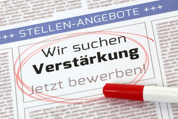Auf einer Seite einer Zeitung ist eine blaue Überschrift mit Pluszeichen und in Großbuchstaben steht "Stellen-Angebote". Darunter der Text "Wir suchen Verstärkung- Jetzt bewerben!".Dieser TExt ist rot umkreist. Auf der Zeitung liegt ein weißer Stift mit einem rotem, geschlossenen Deckel.