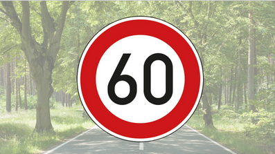 Ein Verkehrsschild mit einem Tempolimit von 60 km/h ist vor einer verschwommenen Straße die von grünen Laubbäumen umgeben ist, abgebildet.