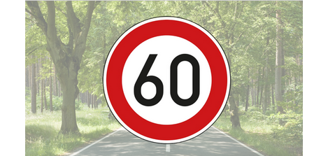 Ein Verkehrsschild mit einem Tempolimit von 60 km/h ist vor einer verschwommenen Straße die von grünen Laubbäumen umgeben ist, abgebildet.