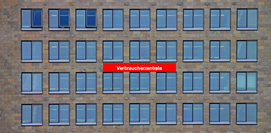 Vierstöckige Büro-Fensterreihe mit gemauerten Steinen und neun Doppelfenstern pro Stockwerk. In der Mitte ein rotes Schild mit den Buchstaben Verbraucherzentrale.