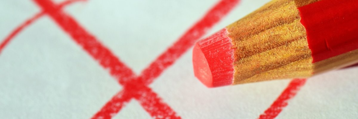 Auf einem weißen Zettel wurde ein rotes Kreuz mit einem Kreis dumrum gemalt. Man sieht den dicken rot beige gestreiften Buntstift mit roter Mine. 