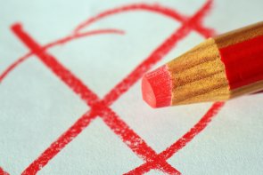 Wahlen Auf einem weißen Zettel wurde ein rotes Kreuz mit einem Kreis dumrum gemalt. Man sieht den dicken rot beige gestreiften Buntstift mit roter Mine.