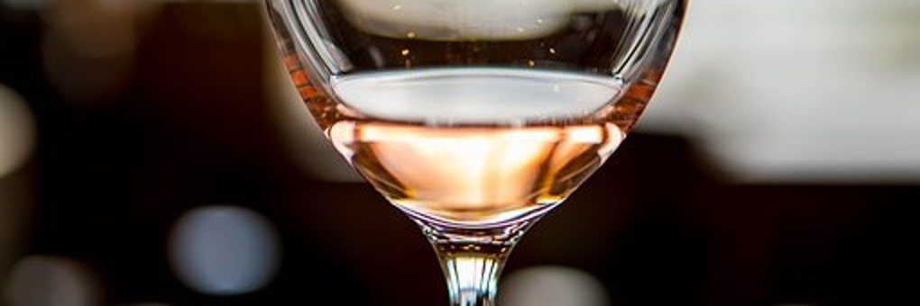 Ein Ausschnitt eines Weinglases, der Stiel und der Kelch. Das Weinglas ist mit Rose gefüllt. Der Hintergrund ist verschwommen. 