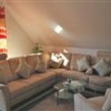 Wohnzimmer mit Dachschräge, beiger U-Couch, Glascouchtisch und rot weiss gestreiften Vorängen