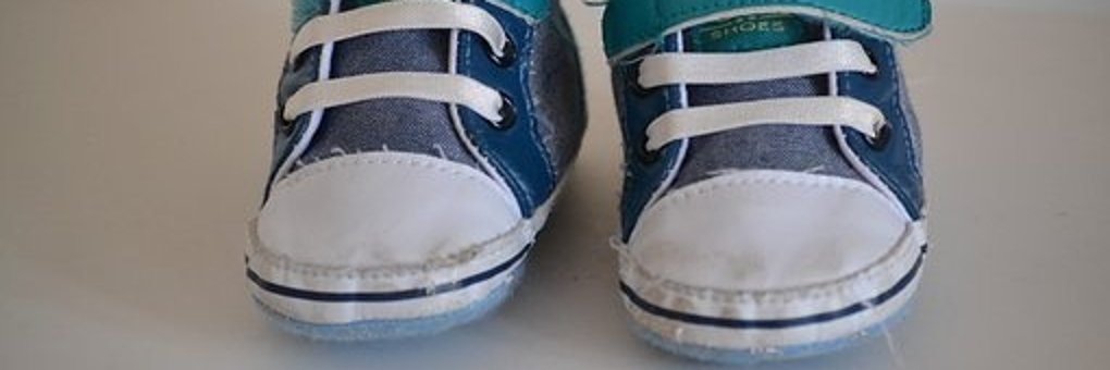 Blau, weiße Babyschuhe mit weißen Schnürsenkel und einem türkisenem Klettverschluss auf einer weißen Tischplatte