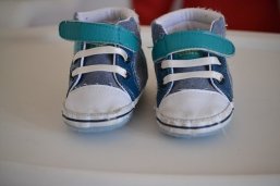 Musterbild weitere Betreuungseinrichtungen Blau, weiße Babyschuhe mit weißen Schnürsenkel und einem türkisenem Klettverschluss auf einer weißen Tischplatte