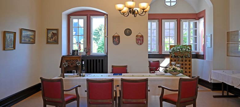 festlich dekorierter Trausaal mit Tisch und Holzstühlen mit rotem Polster
