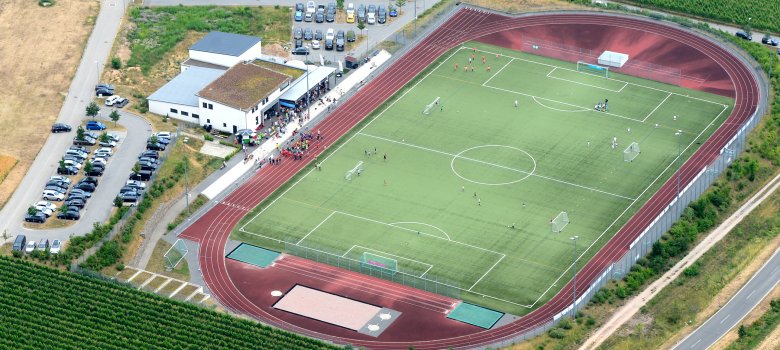 Luftbild der Winfried-Steinmacher-Sportanlage mit Fussballfeld, Laufbahn, Vereinsheim, Parkplätzen und Weinbergen 