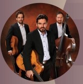 Drei Männer mit weißem Hemd und dunklem Anzug. Zwei haben eine Gitarre in der Hand und ein Mann ein Cello.