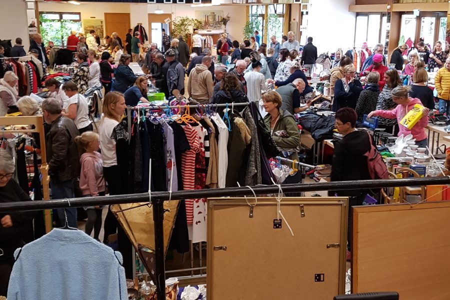 Ein großer Raum mit vielen Leuten und Flohmarktständen mit Tischen und Kleiderstangen.