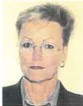Eine Frau mit kurzen, dunkelgrauen Haaren, Creolen, einer Brille und einer grauen Bluse und einem schwarzem Blazer vor einem gelben Hintergrund.