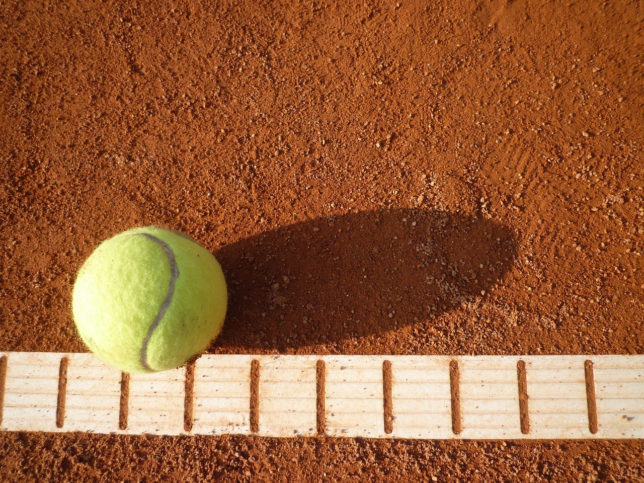 Gelber Tennisball auf roten Boden des Tennisspielfeldes und einer weißen gestreiften Linie.