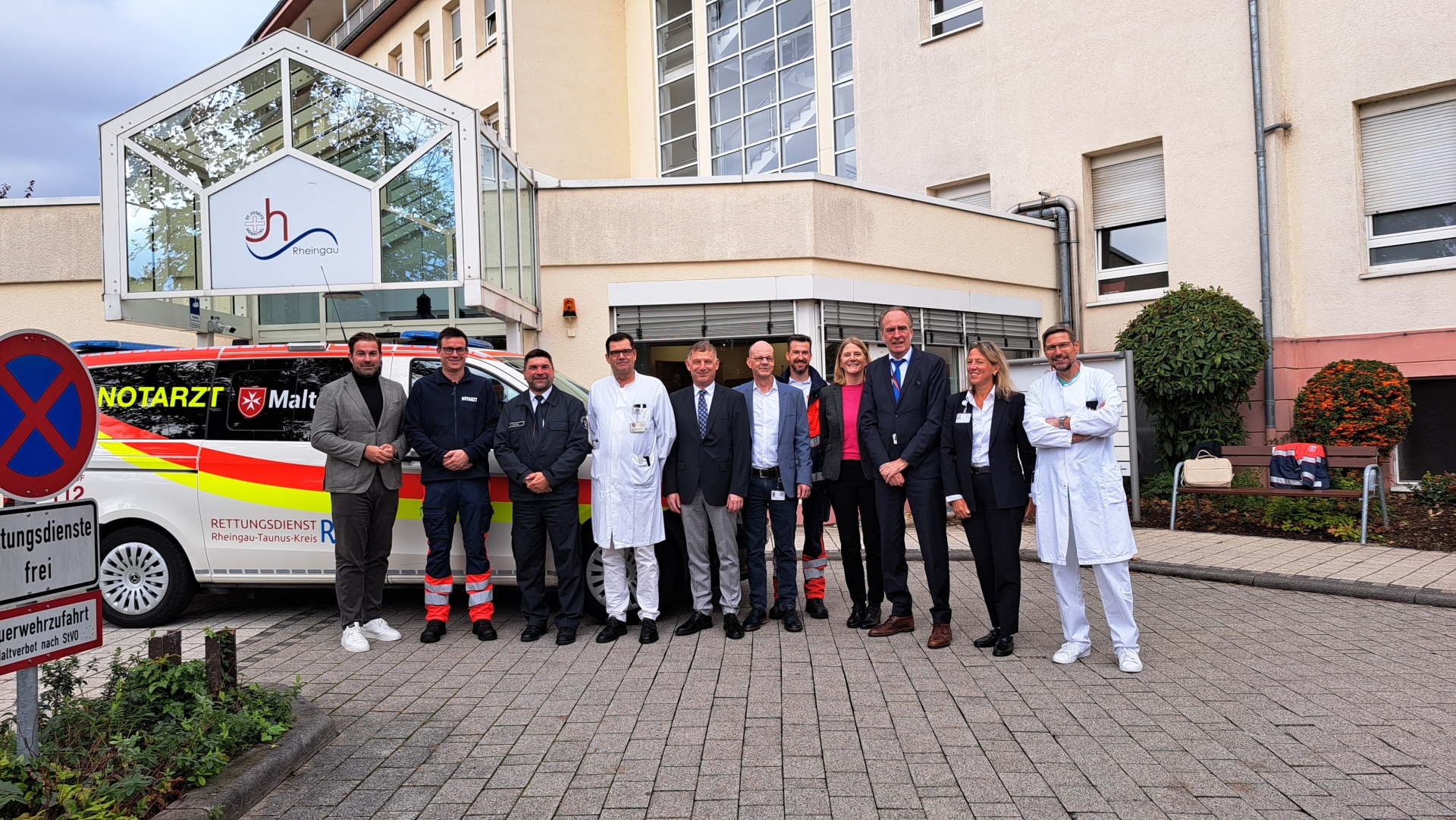 Gruppenbild von Personen wie Ärzte, dem Landrat vor dem Krankhenhaus, im Hintergrund eine Notartzwagen
