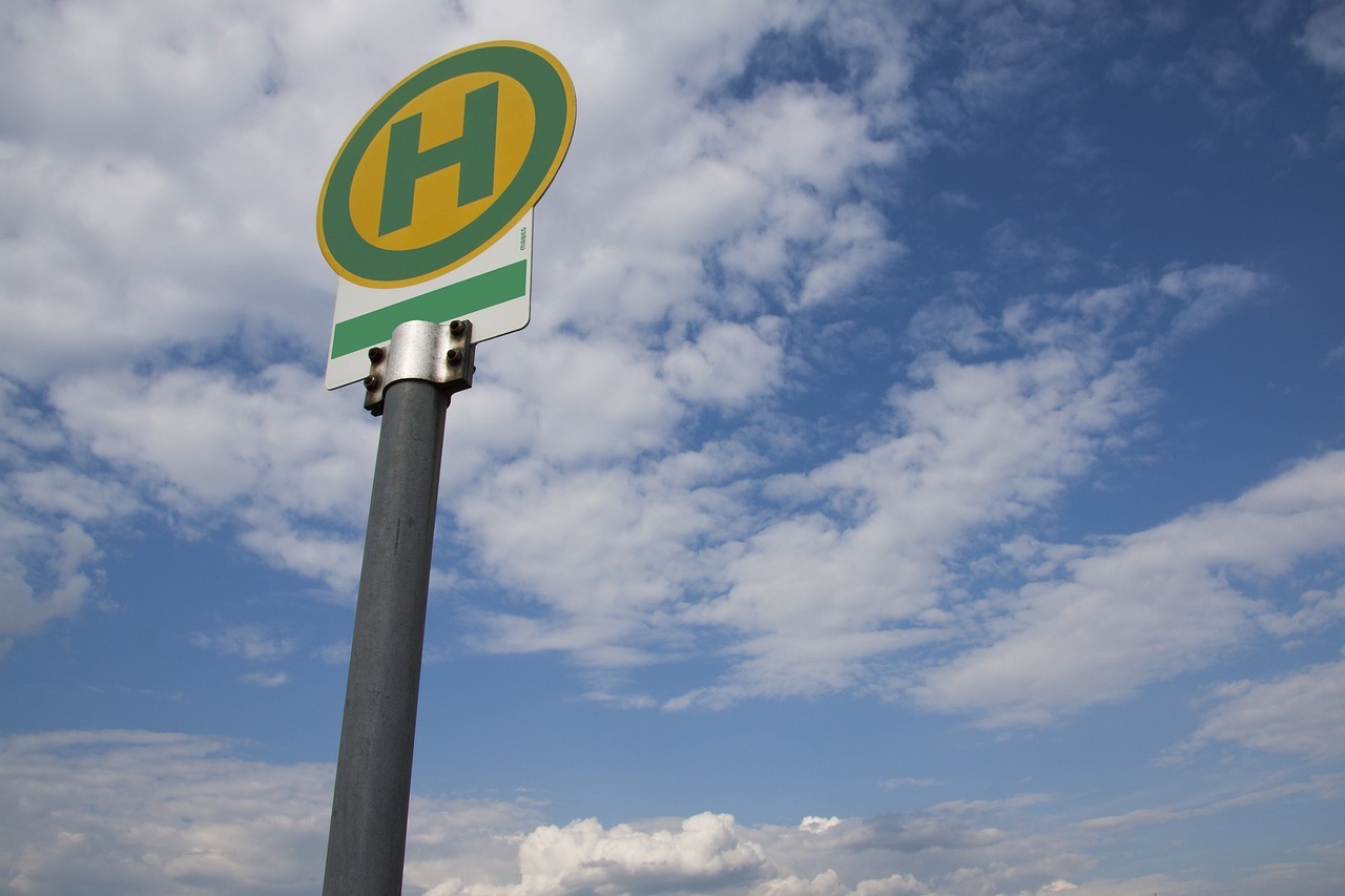 Schild mit grünem H auf gelben Kreis mit Blick in den blauen Himmel mit weißen Wolken.