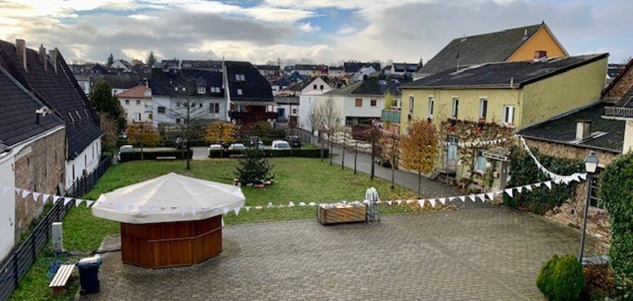 Blick auf den Josef-Staab-Platz mit aufgebautem Glühweinstand und geschmücktem Tannenbaum und einer weißen Wimpelkette auf der Bilder gemalt sind.