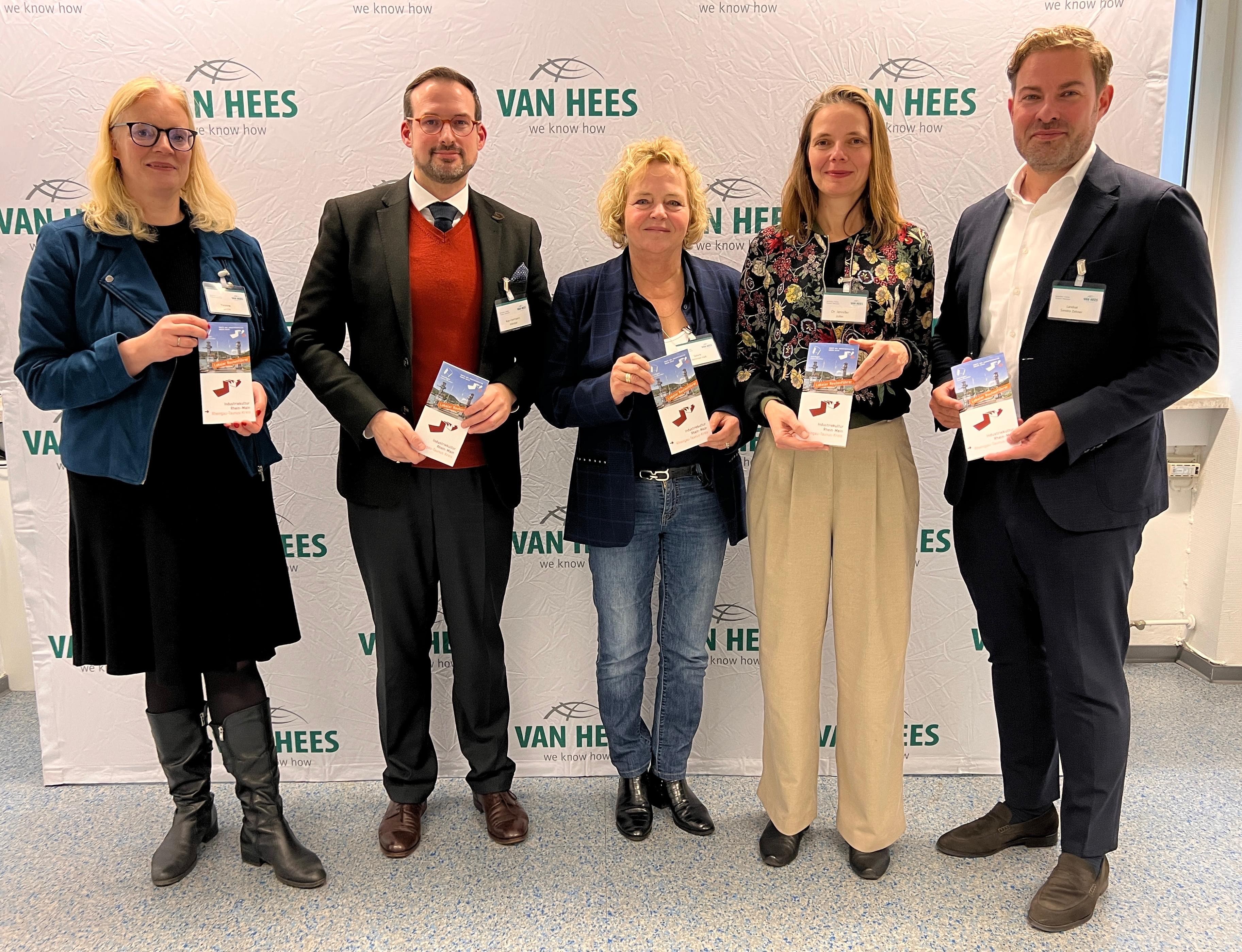 ZWei Damen und drei Herren stehen mit Flyern in den Händen vor einem Werbeplakat.