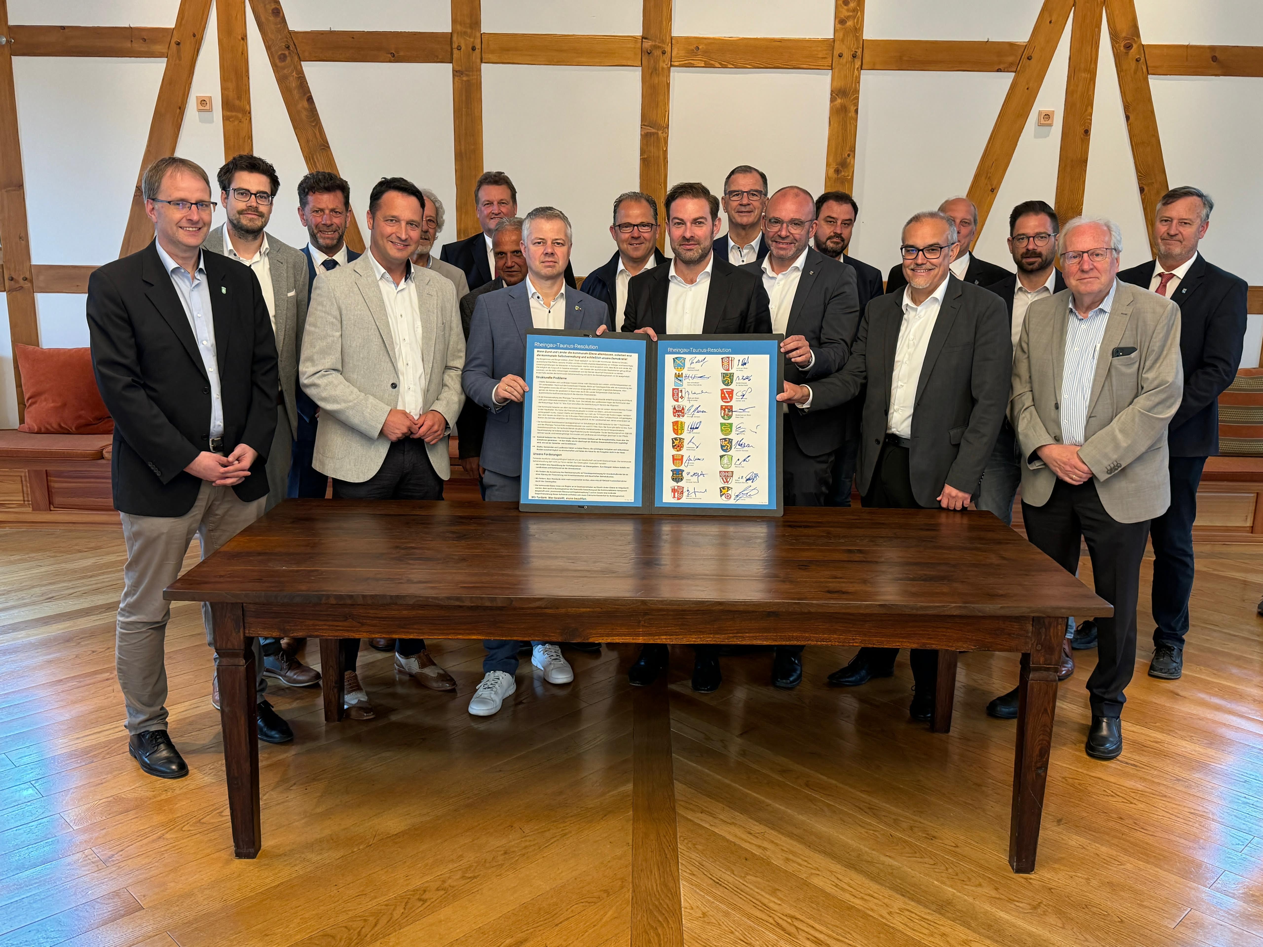 Hinter einem Holztisch stehen die Bürgermeister des Rheingau-Taunus-Kreises und halten die unterzeichnete Resolution in der Hand.